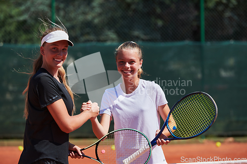 Image of Two female tennis players shaking hands with smiles on a sunny day, exuding sportsmanship and friendship after a competitive match.