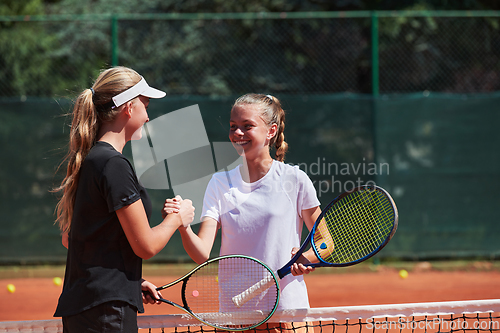 Image of Two female tennis players shaking hands with smiles on a sunny day, exuding sportsmanship and friendship after a competitive match.