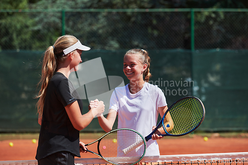 Image of Two female tennis players shaking hands with smiles on a sunny day, exuding sportsmanship and friendship after a competitive match.