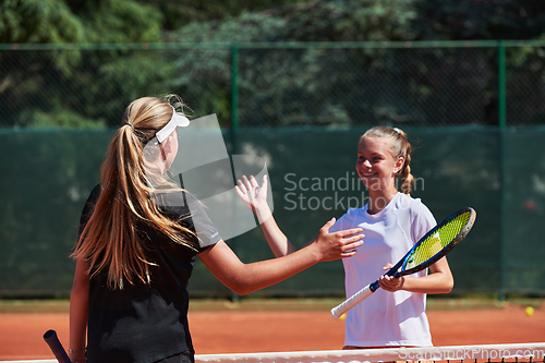 Image of Two female tennis players shaking hands with smiles on a sunny day, exuding sportsmanship and friendship after a competitive match.