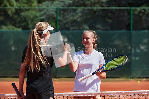 Image of Two female tennis players shaking hands with smiles on a sunny day, exuding sportsmanship and friendship after a competitive match.