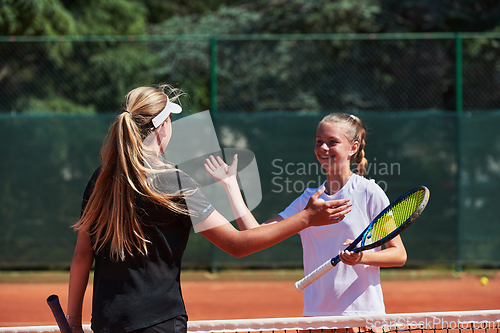 Image of Two female tennis players shaking hands with smiles on a sunny day, exuding sportsmanship and friendship after a competitive match.