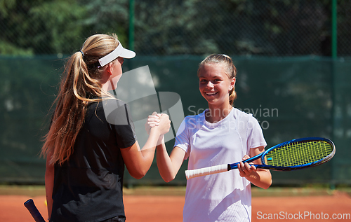 Image of Two female tennis players shaking hands with smiles on a sunny day, exuding sportsmanship and friendship after a competitive match.