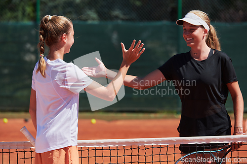 Image of Two female tennis players shaking hands with smiles on a sunny day, exuding sportsmanship and friendship after a competitive match.