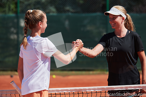 Image of Two female tennis players shaking hands with smiles on a sunny day, exuding sportsmanship and friendship after a competitive match.