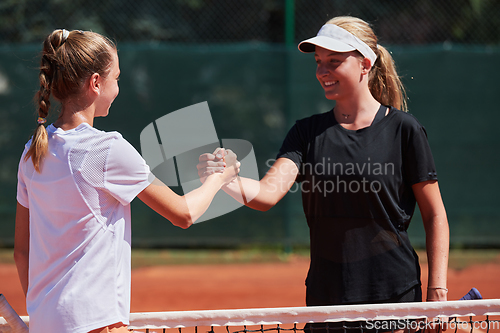 Image of Two female tennis players shaking hands with smiles on a sunny day, exuding sportsmanship and friendship after a competitive match.