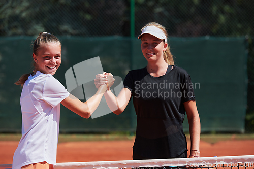 Image of Two female tennis players shaking hands with smiles on a sunny day, exuding sportsmanship and friendship after a competitive match.