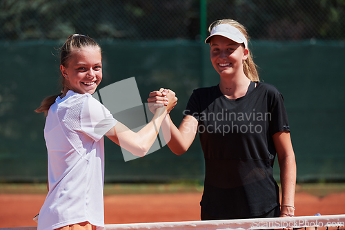 Image of Two female tennis players shaking hands with smiles on a sunny day, exuding sportsmanship and friendship after a competitive match.