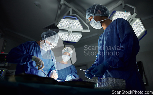 Image of Teamwork, emergency and doctors or people in surgery procedure or healthcare operation in hospital. Night, low angle or surgeon in face mask or gloves help in dark operating room in medical clinic