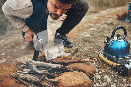 Image of Wood, nature and man with fire on camp for kettle on an outdoor adventure, vacation or weekend trip. Stones, sticks and young male person blowing for flame or smoke in the forest on holiday in Canada