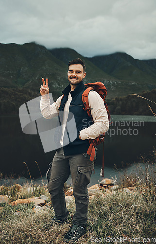 Image of Happy man, portrait and peace sign on mountain for hiking, travel or outdoor backpacking in nature Male person or hiker smile with backpack for trekking, journey or adventure in happiness by the lake