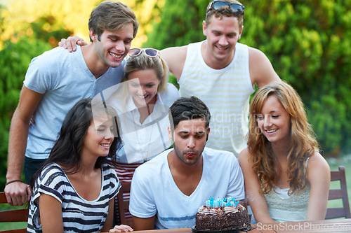 Image of Birthday, friends and blow candles outdoor for celebration, surprise or party with milestone or happiness. Cake, men and women in backyard of home or nature with gathering or social event with smile