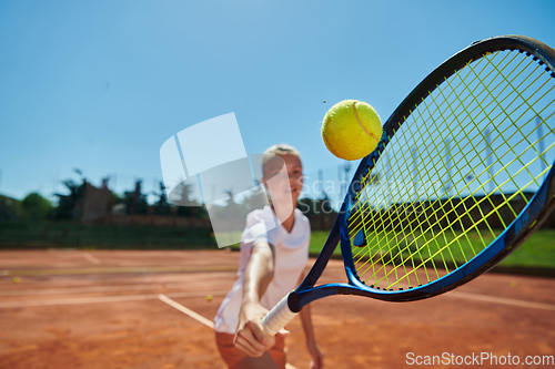 Image of Close up photo of a young girl showing professional tennis skills in a competitive match on a sunny day, surrounded by the modern aesthetics of a tennis court.