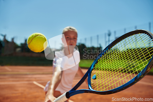 Image of Close up photo of a young girl showing professional tennis skills in a competitive match on a sunny day, surrounded by the modern aesthetics of a tennis court.