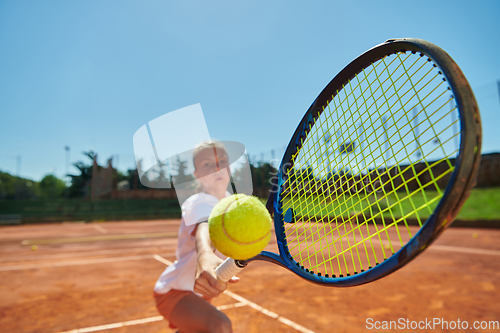 Image of Close up photo of a young girl showing professional tennis skills in a competitive match on a sunny day, surrounded by the modern aesthetics of a tennis court.