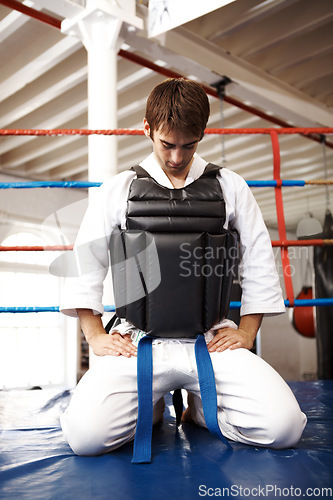 Image of Karate, man and kneeling, exercise with fight in ring and martial arts, protection vest with prayer and ready for battle. Fitness, warrior and muay thai, training and challenge in gym for taekwondo