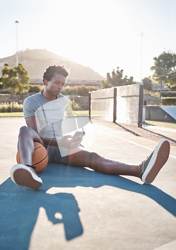 Image of Basketball, phone and man relax on social media, internet and reading news on app outdoor on a court. Black man with 5g smartphone after sport training, exercise and game at sports club in summer
