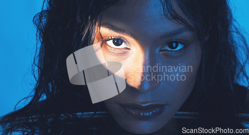 Image of Beauty, cosmetics and portrait of a model with a light reflection on her face in the studio. Spotlight, skincare and young woman from Puerto Rico with natural skin isolated by a blue background.