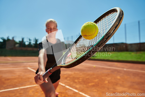 Image of Close up photo of a young girl showing professional tennis skills in a competitive match on a sunny day, surrounded by the modern aesthetics of a tennis court.