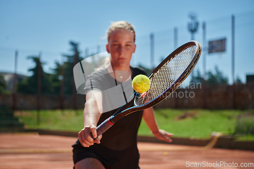 Image of Close up photo of a young girl showing professional tennis skills in a competitive match on a sunny day, surrounded by the modern aesthetics of a tennis court.