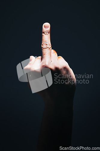 Image of Middle finger, rude and disrespect with the hand of a man in studio on a dark background with light highlight. Angry, sign and gesture with a male showing hatred with an obscene or aggressive symbol