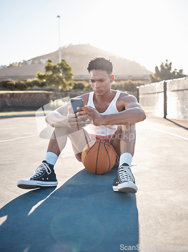 Image of Phone, fitness and basketball man relax typing training results on mobile app, gaming or reading blog update. Basketball player teen on ground and 5g smartphone using phone for social media