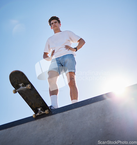 Image of Blue sky, skateboard and young man from below on skate ramp ready for trick. Fitness, street fashion and urban sports, a skater in skatepark and summer sun for adventure, freedom and extreme sport.