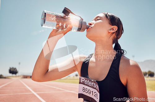 Image of Fitness, water and runner woman training at running track, thirsty and relax after workout against a blue sky background. Sports, girl and drinking water at stadium after running, exercise and sport