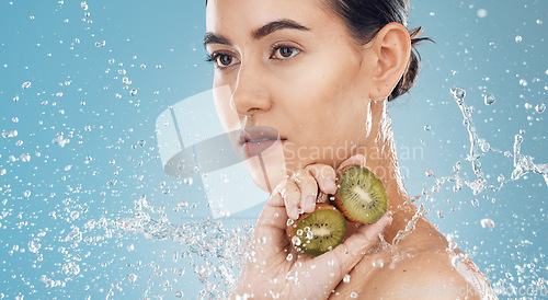 Image of Beauty, water and kiwi with a model woman posing in studio on a blue background for natural skincare with a splash. Food, wet and luxury with an attractive female posing to promote health or wellness