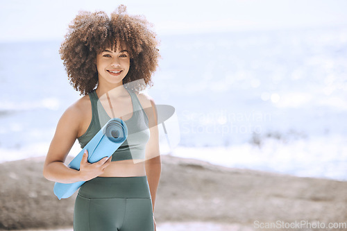 Image of Yoga, fitness and beach with a black woman athlete by the sea with her exercise mat for a workout. Nature, water and health with a female yogi exercising for wellness, zen or mental health outside