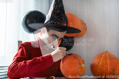 Image of Happy teen boy in costume drawing a pumpkin for the Halloween celebration.