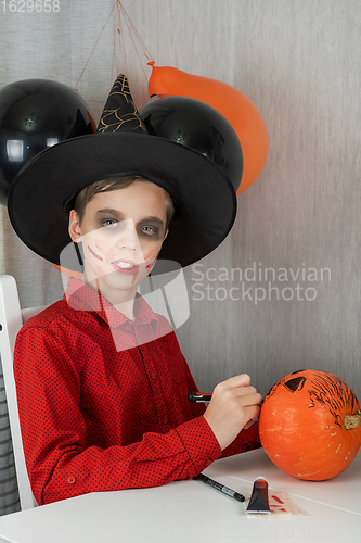 Image of Happy teen boy in costume drawing a pumpkin for the Halloween celebration.