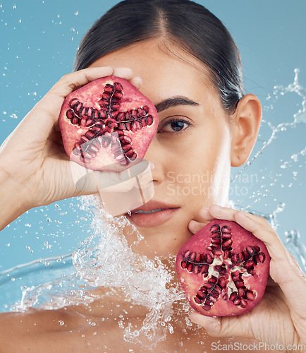 Image of Face, skincare and pomegranate in woman hands with water splash for facial organic, eco friendly or vegan product in studio blue mock up. Model with fruits for glow skin care promotion or advertising