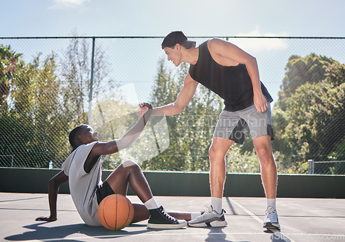 Image of Sports, teamwork and men with helping hand in basketball, player giving support, help and assistance. Fitness, friends and man lifting black man with injury from ground on outdoor basketball court