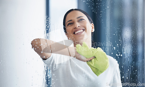 Image of Cleaning, glass and hygiene with a black woman using a cloth or rag while wiping a window in an office. Cleaner, janitor or housekeeper washing a transparent surface with soap and water