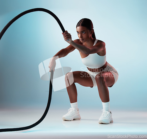 Image of Woman, battle rope and exercise on blue background in studio resistance training, energy sports or cardio workout. Personal trainer, fitness model or person with wellness health goals for arm muscles