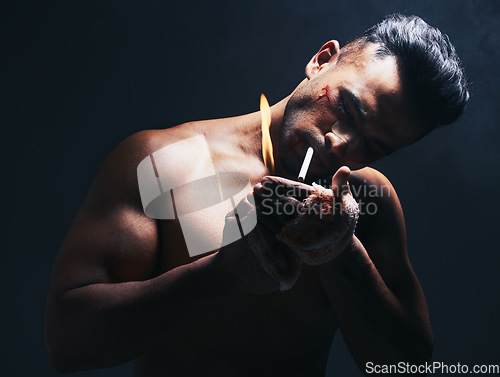 Image of Dark, flame and man lighting a cigarette with a lighter to smoke after a fight in a studio. Young, dangerous and smoker or fighter from Puerto Rico smoking tobacco isolated by a black background.