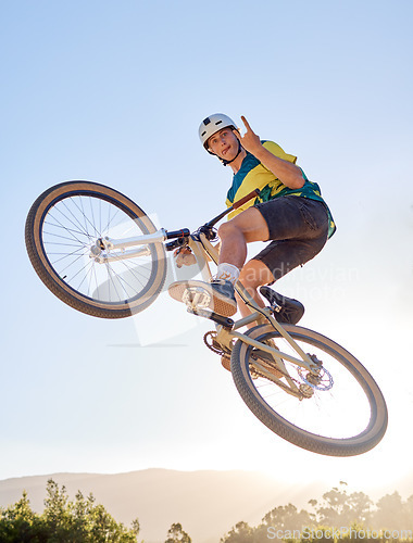 Image of Bike, jump and rock on hand sign with a man bmx rider jumping over a ramp on a trail or course in nature. Sky, mountain and cycling with a male athlete jumping in mid air during fitness exercise