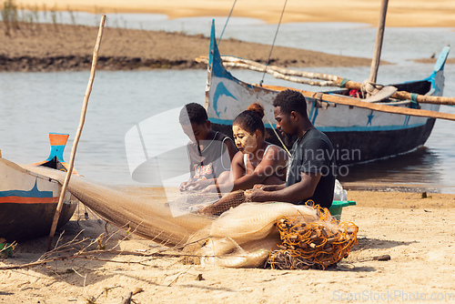 Image of Fisherman and woman repairing fishing nets at the estuaries of a river. The woman has a traditionally Malagasy painted face