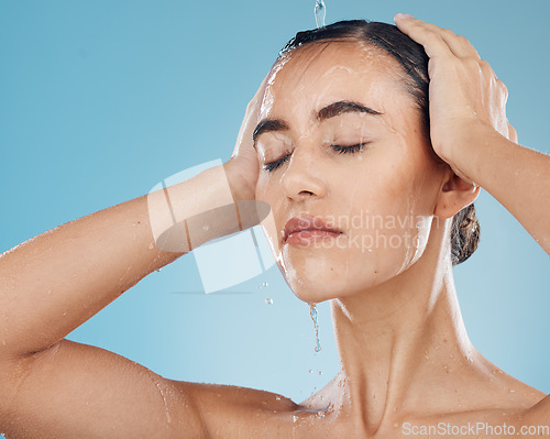 Image of Shower, water and woman cleaning her body on a blue studio background. Bodycare, haircare and health or wellness with a young female cleansing her face, getting wet for fresh and cosmetic skin