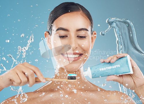 Image of Woman, brushing teeth and with smile, happy and water splash for wellness, dental care and with blue studio background. Oral hygiene, young female and girl being confident, toothpaste and tooth brush