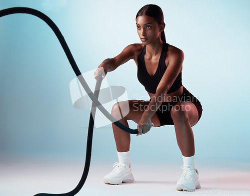 Image of Woman, battle rope or training on blue background in studio for exercise, training or workout for strong arm muscles. Personal trainer, sports person or fitness model in cardio or energy gym wellness