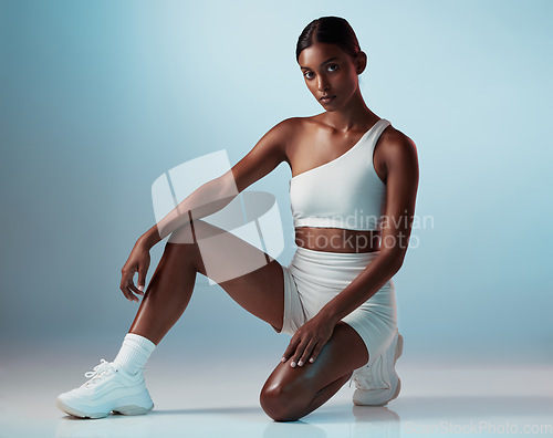 Image of Health, fitness and portrait of woman kneeling isolated on a blue studio background. Sports, exercise and athletic female from India with motivation for wellness ready for serious training or workout