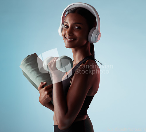 Image of Woman, dumbbells and music headphones for workout in studio on blue background for yoga mat training, exercise or pilates. Portrait, smile or happy fitness model with weights, radio or health podcast