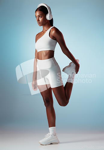 Image of Fitness, music and stretching with woman and headphones for running, training and workout in blue background studio. Energy, freedom and health with girl runner streaming for sports, podcast or audio