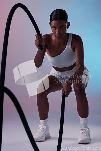 Image of Rope, cardio and woman training for health, fitness and wellness against a colourful studio background. Strong, focus and Indian athlete with battle ropes for exercise, motivation and workout