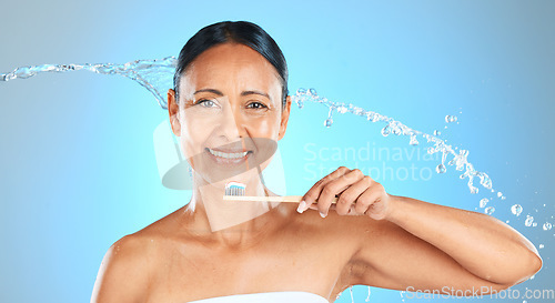 Image of Dental, health and woman brushing teeth with toothbrush, toothpaste and water splash on blue studio background. Healthcare, self care product and oral care hygiene of mature Brazilian beauty model.