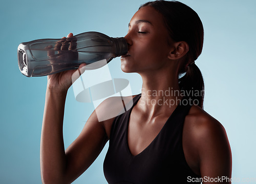 Image of Fitness, sports and woman drinking water in studio for a healthy body after training, cardio workout and exercise. Wellness, blue background and thirsty girl enjoys a beverage to hydrate or hydration