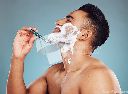 Image of Studio, skincare and man shaving his beard in a daily morning grooming routine with a razor in Mexico. Smile, wellness and happy Latino person shaves his mustache or facial hair for self care hygiene