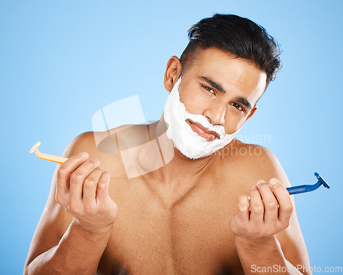 Image of Razor, choice and portrait of man with shaving cream making decision to shave beard in studio. Clean, hygiene and guy from India with doubt and shavers to groom face hair isolated by blue background.